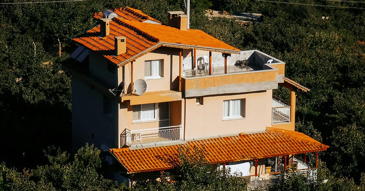 Three-story house with orange roof, balconies, and rooftop terrace surrounded by greenery.